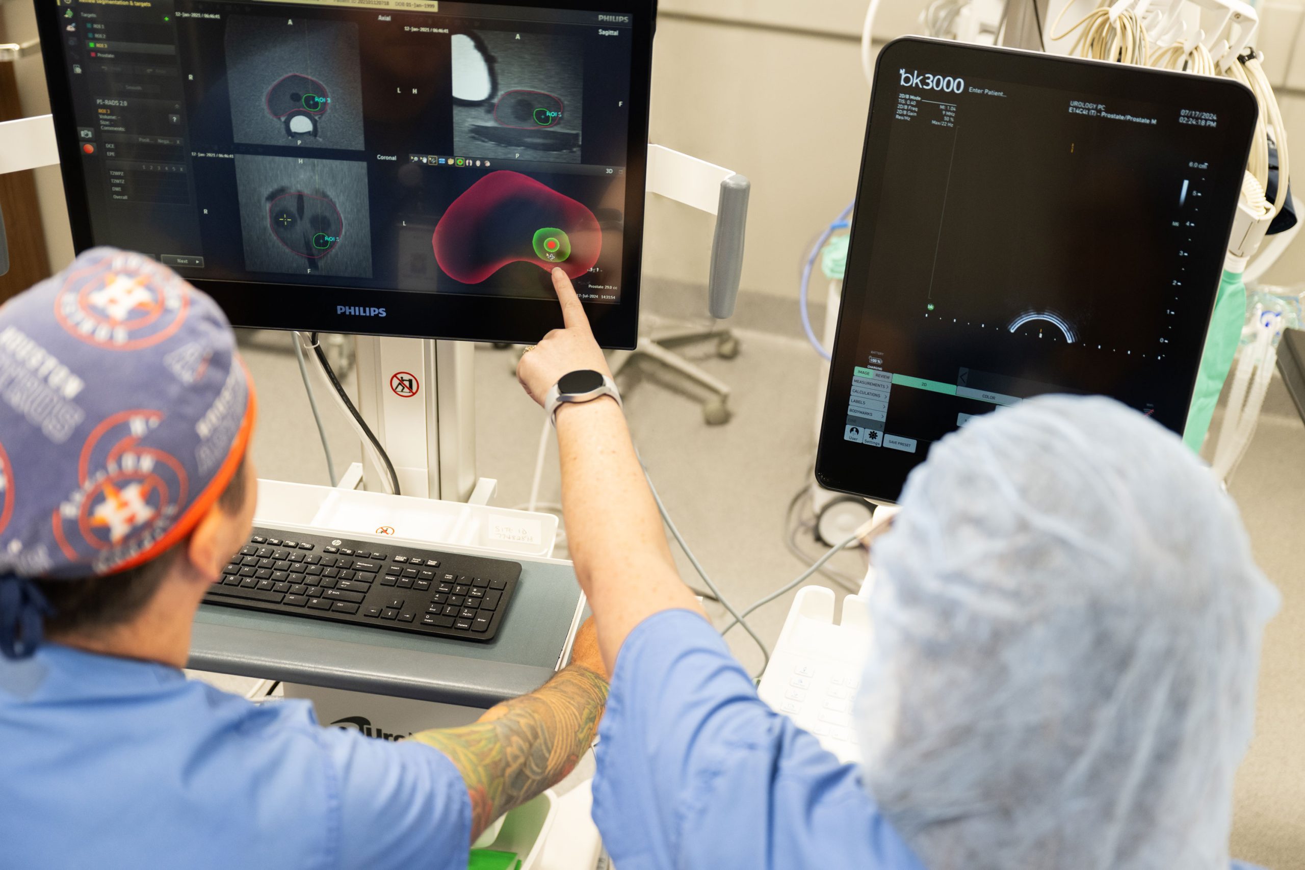 Two people in scrubs pointing at a screen with an MRI on it