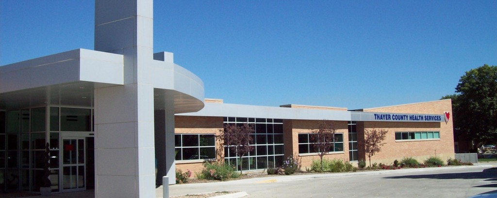 Front entrance of Thayer County Health Services building with stone walls and many windows in Hebron, Nebraska