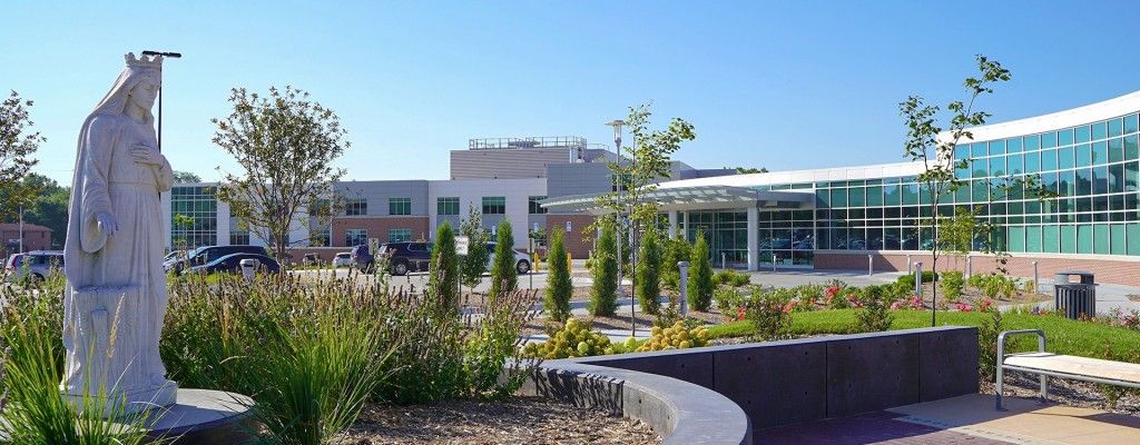 Front entrance of Madonna Rehabilitation Hospital with drive-under awning, green windows, and lots of greenery and plants in Madonna, Nebraska