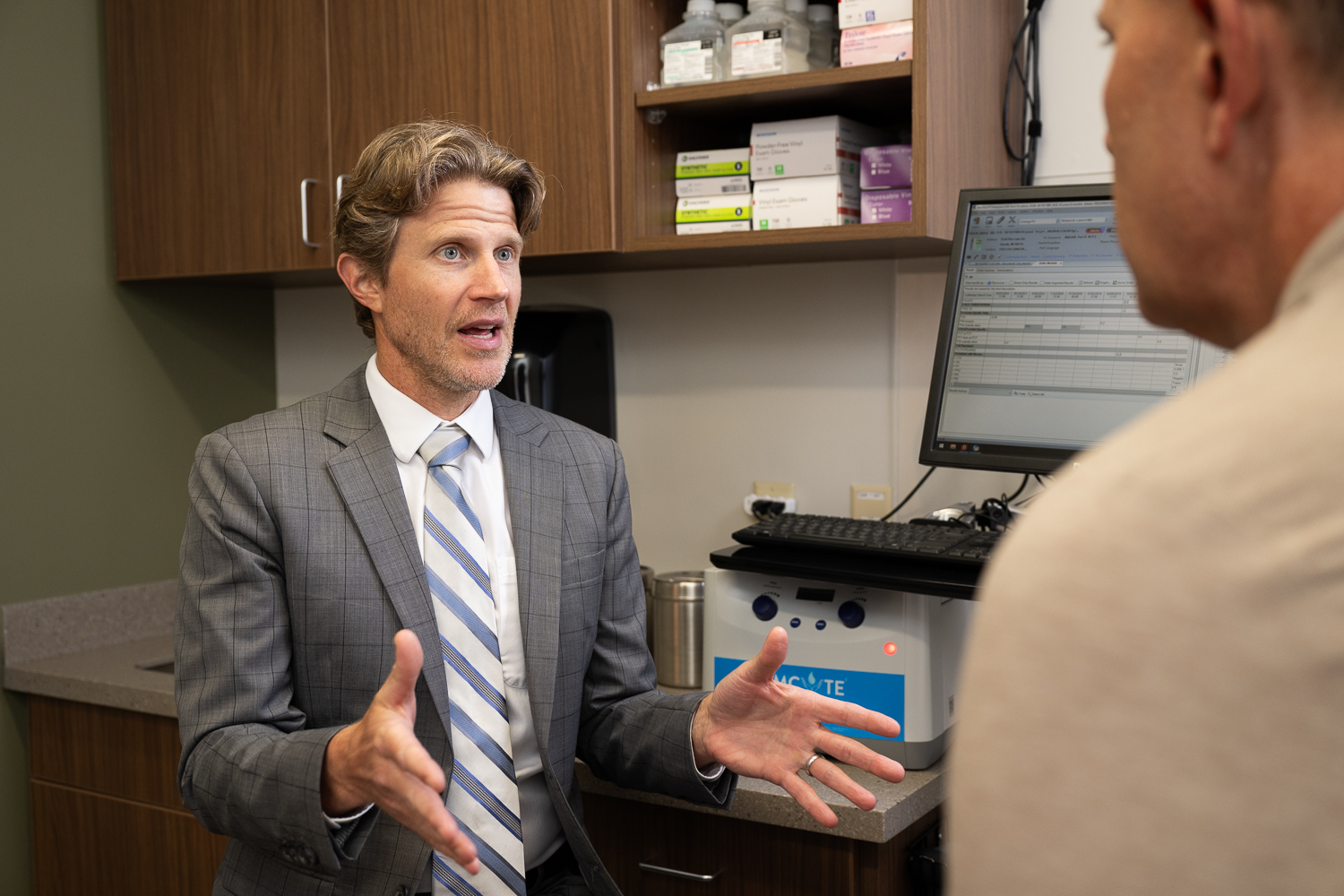 Man in a suit and tie in a doctors office explaining something to a patient