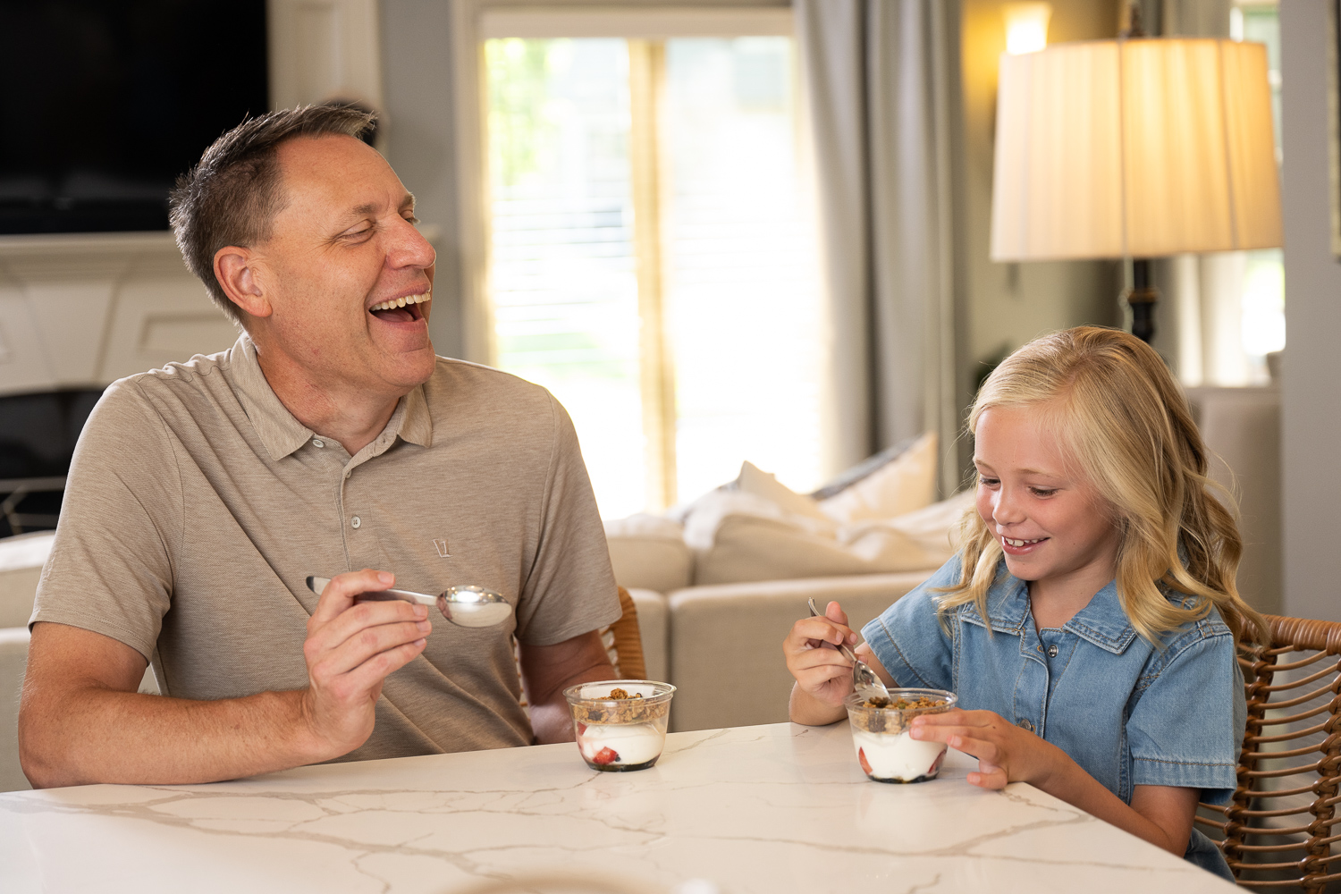 Older man and young girl sitting at a table eating yogurt parfaits and laughing